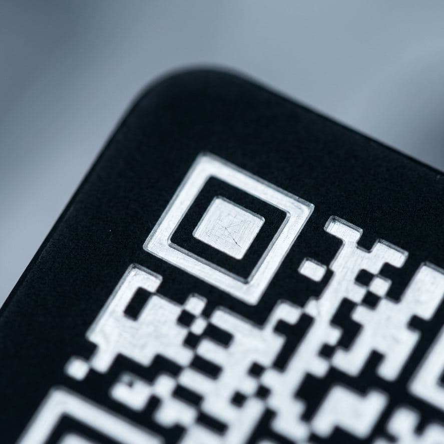 Laser-etched 2D Data Matrix code on a black anodized aluminum panel — high-contrast white modules exposed where the anodized layer was removed.